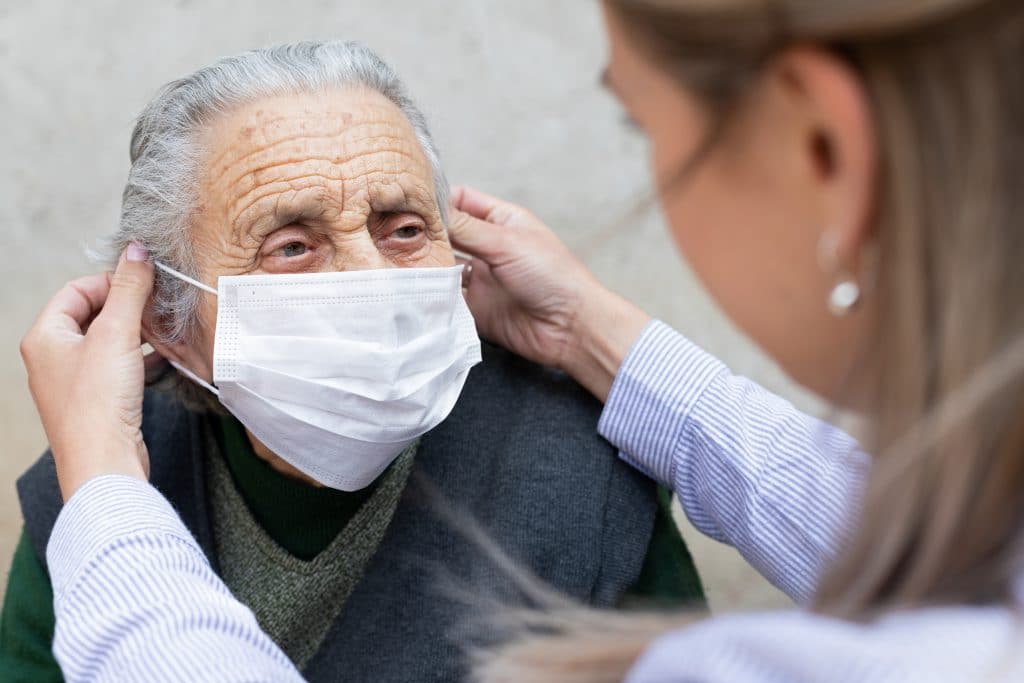 Nurse putting on mask on elderly woman
